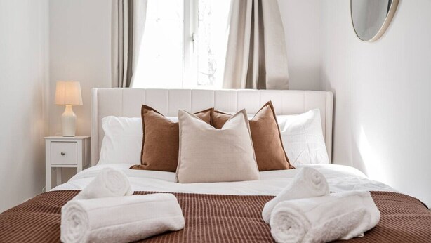 Een opgemaakt bed met een bruine sprei, witte kussens en twee opgerolde handdoeken.