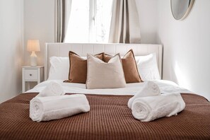 A neatly made bed with a brown bedspread, white pillows, and two rolled towels on the bed. - Charming Suffolk Cottage, 3 Bedroom + Parking (Blyford)