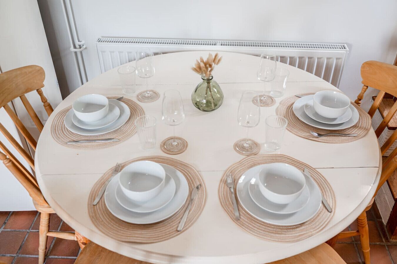 A round dining table set with plates, bowls, and cutlery, surrounded by wooden chairs.