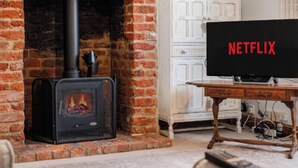 Een woonkamer met een open haard van baksteen, een televisie en een kast.