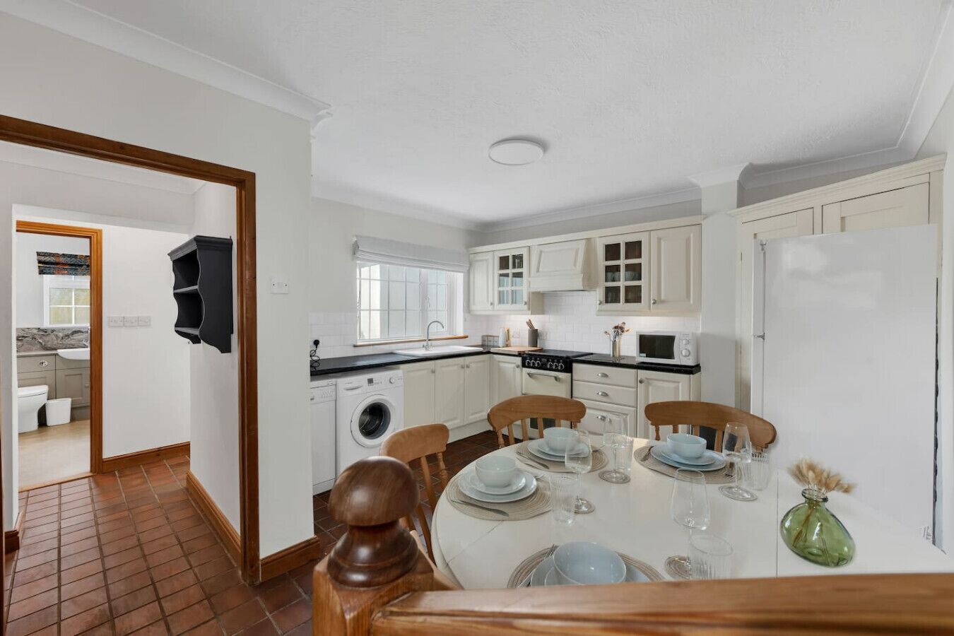 Una cocina compacta con armarios blancos, lavadora y comedor con mesa dispuesta para cuatro.