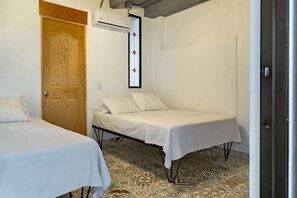 A room with two beds, a wooden door, an air conditioning unit, and a patterned floor.