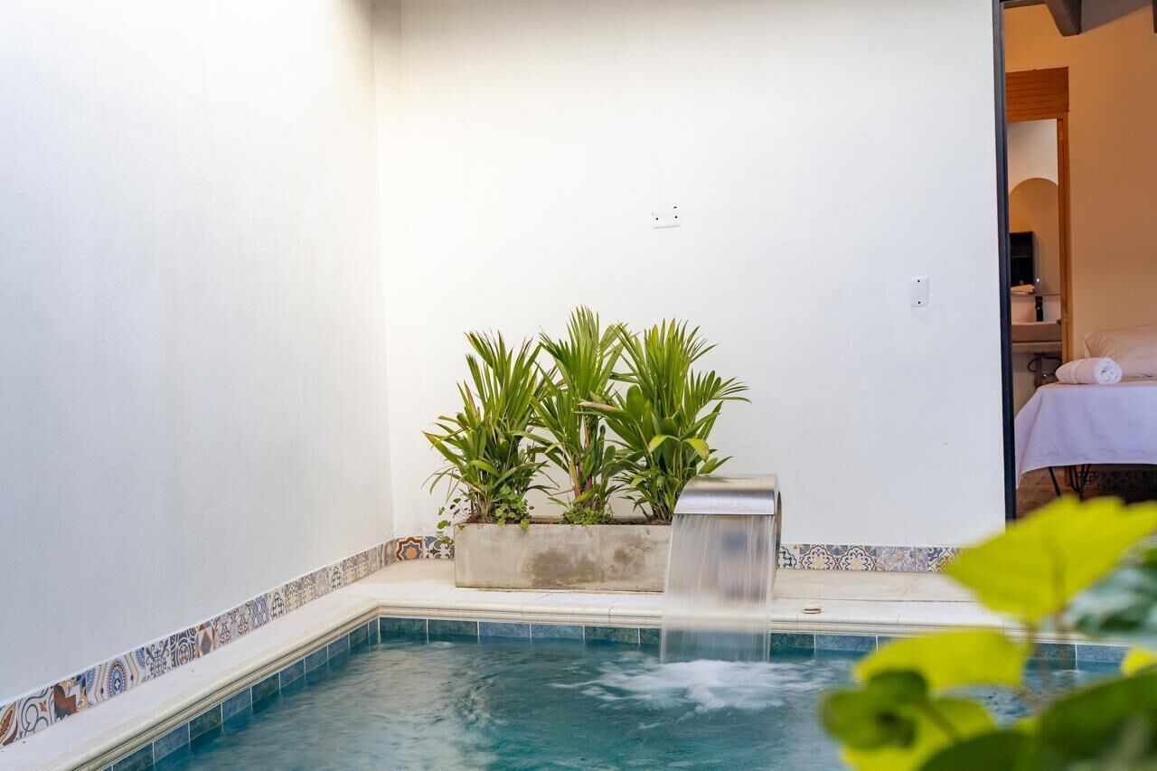 A small pool with a waterfall feature, surrounded by white walls and a tiled border.