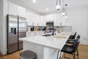 Een moderne keuken met witte kasten, roestvrijstalen apparatuur en een centraal eiland met stoelen.