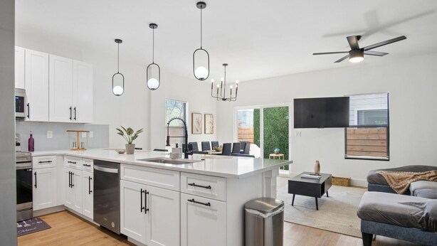 A modern kitchen with white cabinets, a central island, pendant lights, and a ceiling fan. - Stylish Downtown Retreat Near the Alamodome (San Antonio)