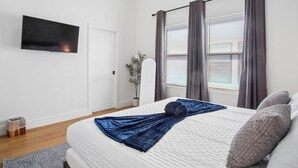 A bedroom with a bed, a TV, a window with curtains, a potted plant, and a door. - Stylish Downtown Retreat Near the Alamodome (San Antonio)