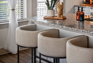 A kitchen with a granite countertop, three bar stools, a potted plant, and a wooden sculpture. - Lux 2 Bd/2 Bath /Ceder Springs/Free Parking/Gym/Pool (Dallas)