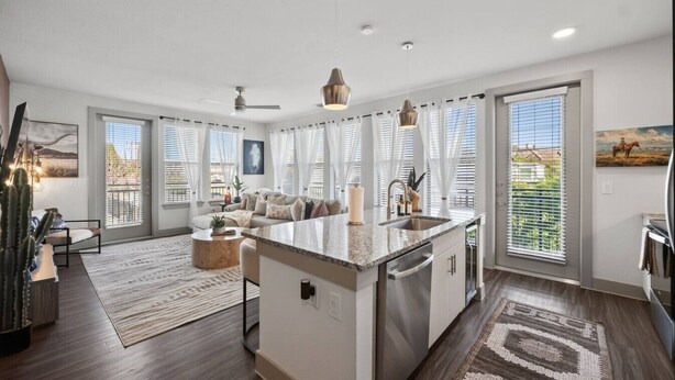 Eine moderne Küche mit einer zentralen Kochinsel, einem Essbereich mit einer Sitzecke und großen Fenstern mit Jalousien.