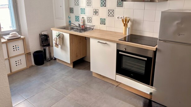 A modern kitchen with a stainless steel refrigerator, an oven, a sink with a faucet, and a window with blinds. - Apartment T2/3 Corte center (Corte)