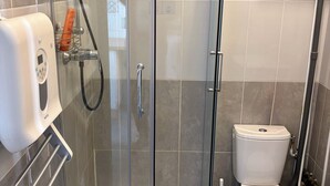 A glass-enclosed shower with a handheld showerhead, a toilet, and a soap dispenser. - Apartment T2/3 Corte center (Corte)