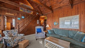 Ein Holzblockhaus-Interieur mit Treppe, Sofa, Sessel und einer an der Wand hängenden Karte.