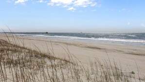Ein Strand mit Dünen, einem Steg, der sich ins Wasser erstreckt, und einem klaren Himmel.
