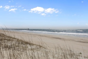 Une plage avec des dunes de sable, une jetée qui s’avance dans l’eau et un ciel dégagé.