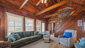 Ein Holzinterieur mit einer Couch, Sesseln, einer Treppe und einem Wandbild.