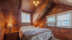 Ein Schlafzimmer einer Holzhütte mit Bett, Nachttisch, Lampe und Fenster mit Jalousien.