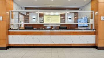 A hotel reception desk with a marble countertop, wooden paneling, and a large digital display.