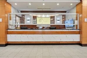 Un comptoir d’accueil d’hôtel doté d’un plan de travail en marbre, de panneaux en bois et d’un grand écran numérique.