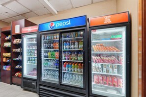 Une rangée de distributeurs automatiques de boissons arborant le logo Pepsi, entourés d’étagères remplies d’en-cas et d’autres produits alimentaires.