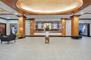 Un hall d’hôtel comprenant un comptoir d’accueil, un espace salon et un grand lustre circulaire au plafond.