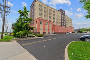 A multi-story hotel with a red and beige facade, a parking lot, and a clear sky. - Near NYC • Superior King Suite • Premium Comfort • Workspace (Carteret)