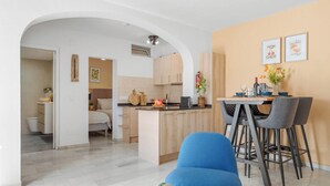 Eine moderne Küche mit Holzausstattung, ein Essbereich mit Tisch und Stühlen sowie ein sichtbares Badezimmer mit einem Bett.