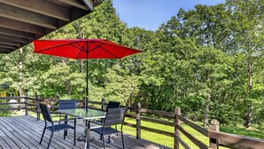 Une terrasse en bois avec une table et des chaises en verre, un parasol rouge et une clôture en bois.