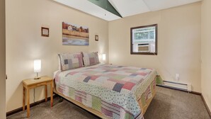 Une chambre à coucher avec un lit, une table de chevet, un ventilateur de plafond, une fenêtre et un tableau au mur.