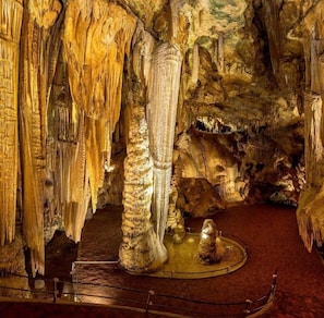 Eine Höhle mit Stalaktiten, einer großen Säule und einer Plattform mit einer Statue.