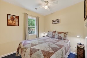 A bedroom with a bed, a ceiling fan, a window with curtains, and two wall-mounted pictures. - Shenandoah Retreat / Walk to river / dog friendly (Page County)