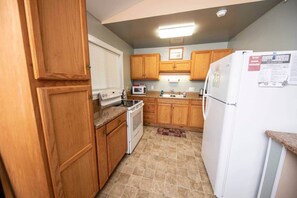 A compact kitchen with wooden cabinets, a microwave, an oven, and a refrigerator.