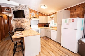 A kitchen with a stone accent wall, wooden cabinets, a microwave, a refrigerator, and a wooden dining table with chairs. - Serene mountain getaway / Beautiful Views / Dog friendly (Page County)
