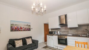 Eine moderne Küche mit weißen Schränken, einem eingebauten Backofen und einer Mikrowelle. Ein graues Sofa mit floralen Kissen und ein Blumenbild an der Wand.
