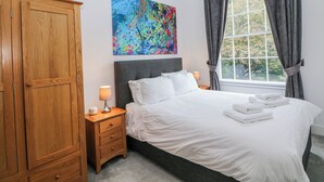 Ein Schlafzimmer mit einem Bett, einem Nachttisch, einem Holzschrank, einem farbenfrohen abstrakten Gemälde und einem Fenster mit Vorhängen.