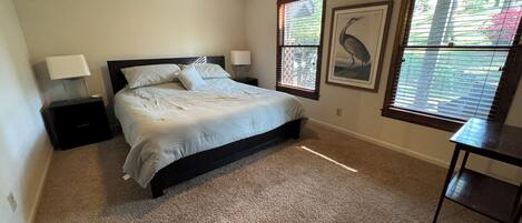 A bedroom with a bed, two bedside tables, a ceiling fan, and two windows with blinds.