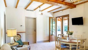 Una habitación con techo de madera, una mesa de comedor con sillas, un sofá, una lámpara y un televisor montado en la pared.