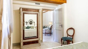 Un dormitorio con una cama, un espejo grande, una silla y una puerta que da a otra habitación.
