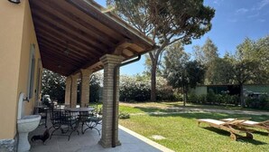 Un patio cubierto con una mesa y sillas, una pérgola de madera y un césped con un árbol.