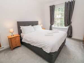 A neatly made bed with white linens, a bedside table with a lamp, and a window with curtains. - Abraham (Matlock)