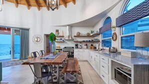 Eine moderne Küche mit weißen Schränken, einem Holztisch und Blick auf das Meer.