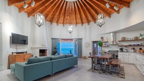 Ein modernes Wohnzimmer mit Holzboden, einer Couch, einem Fernseher und einem Essbereich mit Meerblick.