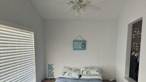 A bedroom with a bed, a ceiling fan, a window with blinds, a bedside table, and a wall-mounted sign. - 2-bedroom house in peaceful Surfside Beach and beautiful view of the gulf (Surfside Beach)