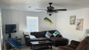 A living room with a ceiling fan, a TV, a sofa, a coffee table, and a blue chair. - 2-bedroom house in peaceful Surfside Beach and beautiful view of the gulf (Surfside Beach)