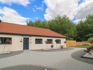 A single-story building with a red-tiled roof, a front door, and windows. There is a paved driveway leading to the entrance, and a wooden fence in the background. - Maple Lodge (Bridgwater)