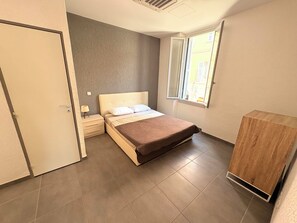 Une chambre à coucher comprenant un lit, une table de chevet, une lampe, une fenêtre et une armoire en bois.