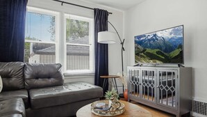 A living room with a grey sofa, a coffee table with decorative items, a cabinet with glass doors, and a large TV on a stand.