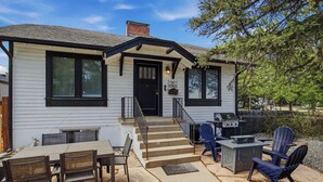 A house with a front porch, a dining area with chairs and a table, and a barbecue grill outside.