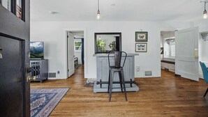 A spacious room with a wooden floor, a dining area with a bar, and a large window.