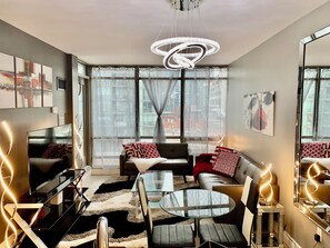 A modern living room with a glass coffee table, sofas, a TV, and a large window with curtains. - Toronto Glamour (Toronto)