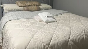A neatly made bed with a quilted duvet, pillows, and a folded towel.