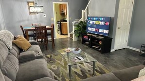 A living room with a sofa, a coffee table, a TV, and a staircase leading to a kitchen.